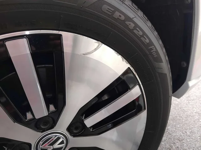 Two-tone Volkswagen wheel before cosmetic repair, with visible damage along the outer rim edge